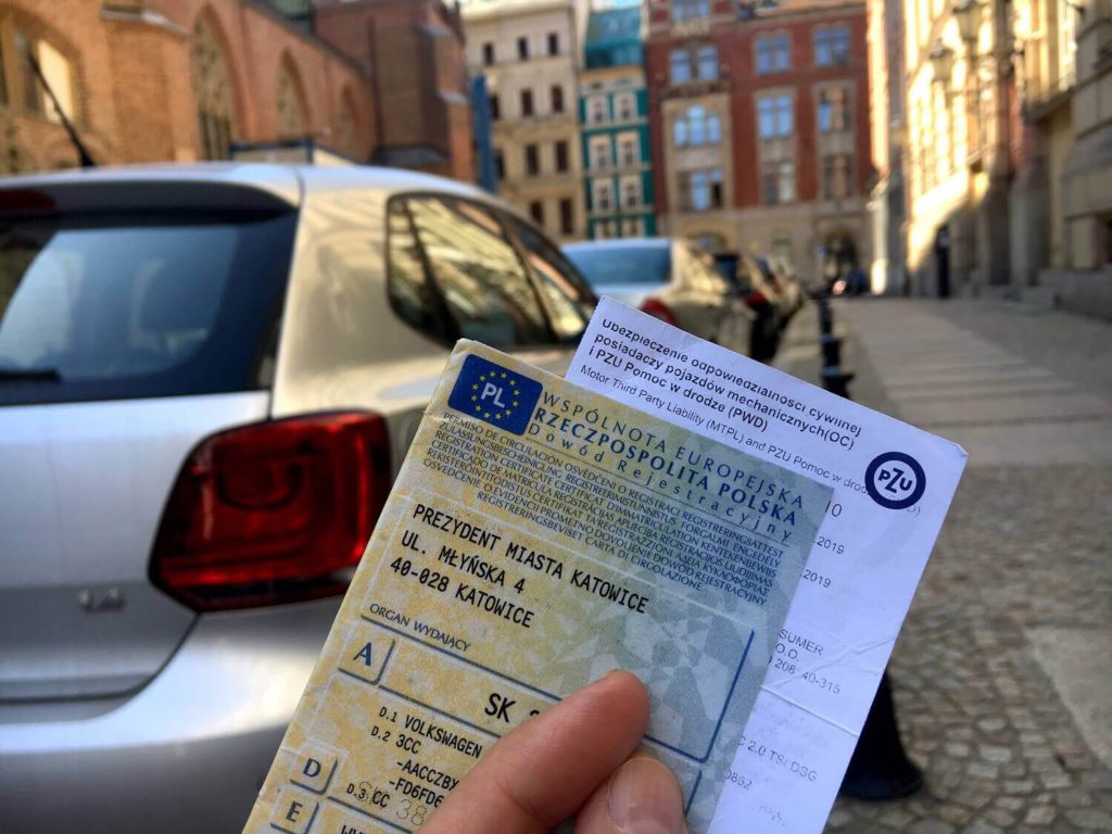 Dokumenty samochodowe na tle zaparkowanego auta - OC na raty 2025 i najtańsze oferty