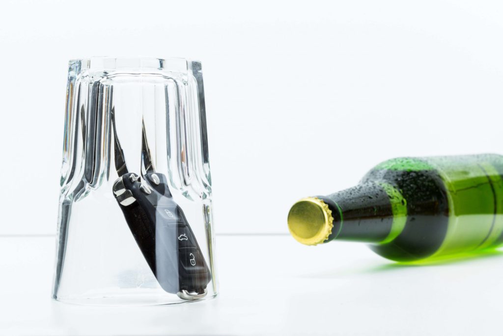 Symbolicznie: butelka piwa i kluczyki samochodowe pod szklanką – wpływ alkoholu na wypadki drogowe