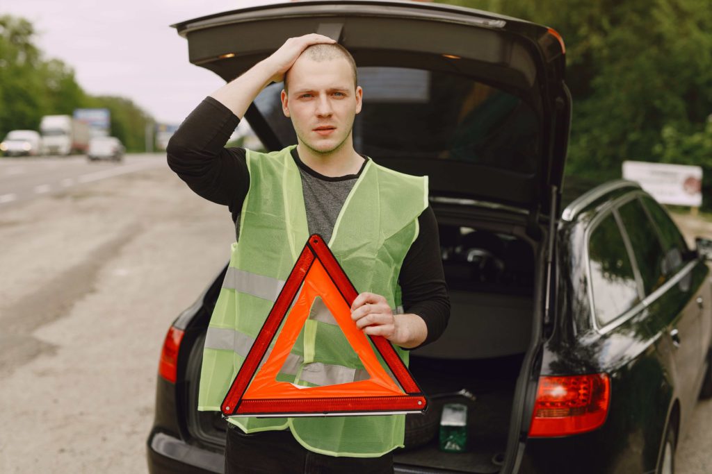 Kierowca w kamizelce odblaskowej trzymający trójkąt ostrzegawczy – jak zachować się przy awarii samochodu na autostradzie