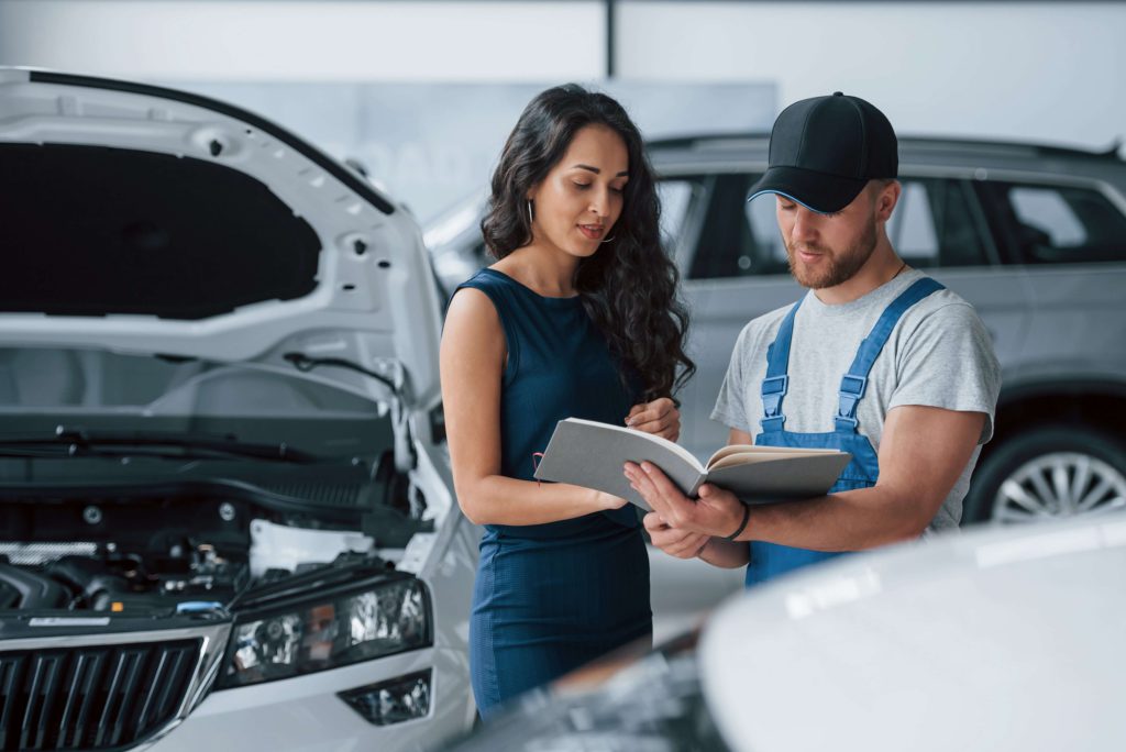 Kobieta rozmawiająca z mechanikiem przy otwartej masce auta – kiedy kierowca nie traci zniżek z ubezpieczenia AC