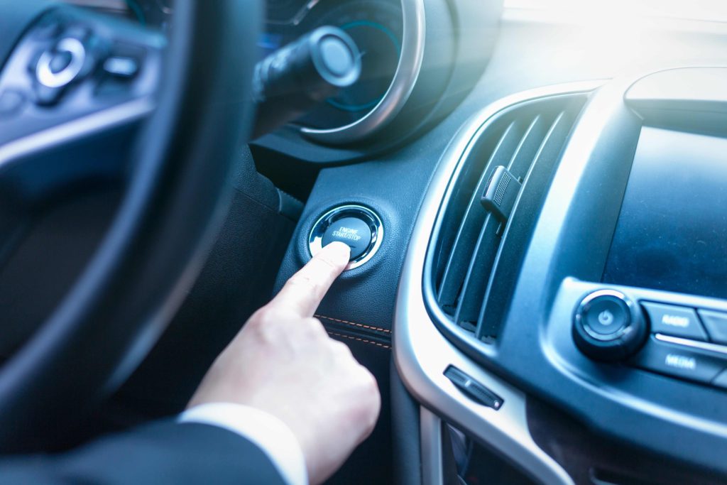Kierowca naciskający przycisk start-stop w samochodzie – jak działa system start-stop i jakie ma wady oraz zalety
